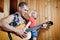 Baby girl with his hipster father playing guitar on wooden background