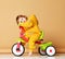 Baby girl kid toddler riding her first bicycle tricycle in warm yellow overalls looking up on warm brown