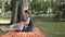 A baby girl in the lap of a young nanny sitting on a blanket spread over grass