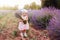 A baby girl looking with curiosity and hold a bouquet of flower on her hands on a rural flower field with lavender