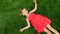 Baby girl is lying on green grass, top view. The child makes an angel like in the snow