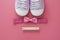 Baby girl pink background with newborn shoes, bow and Welcome words. Baby flat lay