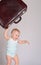 Baby girl playing with suitcase on grey background