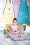 Baby girl plays a wigwam. Scandinavian interior and textiles for the nursery. Happy baby plays in a tent in a children`s room. lit