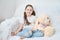 Baby girl sitting on white sofa in white t-shirts and blue jeans. Soft plush banny