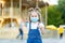 A baby girl stands in an amusement Park wearing a protective medical mask and gives a thumbs up