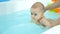 Baby girl swims in bathtub with swim teacher assistance