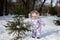 Baby girl wear child snowsuit on a sunny frosty winter day near Christmas tree