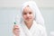 Baby girl, in white robe and towel on her head, in bathroom, holding toothpaste and brush in hand
