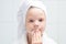 Baby girl, with a white towel on her head, cleans her face with a round cotton swab, close-up, on the background of the bathroom