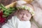 Baby girl in a wicker basket of vine decorated with burgundy peonies in a light winding and a flower wreath on her head.