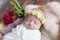 Baby girl in a wicker basket of vine decorated with burgundy peonies in a light winding and a flower wreath on her head.
