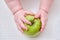 Baby hand and green apple fruit, close-up. Children fingers and an object on a white background