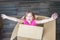 Baby has fun in the mail box. The child screams and waves his arms while sitting in a cardboard box. A little girl prepared a