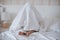 Baby hiding under a white blanket, sitting on the bed.