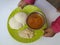 Baby Holding in Hand Home Made Indian vegetarian rice cakes breakfast known as idli or idly, served with sambar and Chatney in a