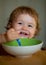 Baby holding a spoon in his mouth. Happy child eating himself with a spoon. Launching child eating food.