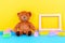 Baby kids toys background with empty picture frame, teddy bear and colorful building blocks bricks