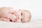 Baby lies on a bed on a white background with a hand in his mouth. Teething. Four month old baby. A child nibbles his hand.