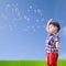 Baby little asian boy standing against blue sky with soap bubble