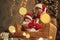 Baby is on the little sofa. Two kids in Santa hats are celebrating holidays indoors together