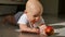 Baby is lying on the floor and holding a red apple. The child is very lively and cheerful, he actively knocks with hands