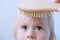 Baby, part of the face, funny brown eyes close-up, mom is combing the girl`s fair hair, concept of baby hygiene, baby hairstyle,