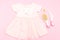 Baby pink dress for a girl and care items on a pink background.