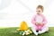 Baby in pink fluffy costume sitting near yellow ostrich egg, colorful chicken eggs and tulips  on white