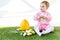 Baby in pink fluffy costume sitting near yellow ostrich egg, colorful chicken eggs and tulips  on white