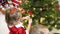 Baby and pregnan mom hang red ball toy on Christmas tree. happy childhood concept. child and mother decorate tree with