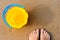 Baby`s bare feet on a golden sandy beach next to a yellow toy bucket. Vacation concept