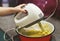 The baby`s hands stir the dough with an electric mixer in the kitchen. A little girl helps her mom make dough with eggs for baking