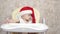 Baby santa claus is sitting on children`s chair and laughing. Child in red santa hat is playing in children`s room. Kid