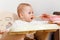 The baby sits in child`s chair for feeding and eats a spoonful of puree. children\\`s appetite