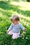 Baby sits on his knees on a green lawn among white flowers