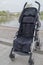 Baby stroller with black quilted fabric seat, standing with wheels on concrete path and on curb on background of rounded city pond