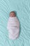 Baby swaddled in white blanket while resting on blue sheets