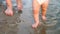 Baby takes first steps along river bank, splashing water in sides and walking along with his mom. Legs. Close-up. Slow