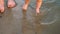 Baby takes first steps along river bank, splashing water in sides and walking along with his mother. Legs. Close-up