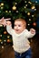 Baby takes first steps holding her mother\'s hand on the background of the Christmas tree