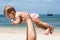 Baby is teething in dad arms. On a tropical beach. Sunny day, father throws up infant toddler, hold on hands. Child enjoyed