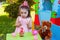 Baby toddler girl in outdoor second birthday party clapping hands at cake with Teddy Bear as best friend
