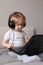 baby todler baby blonde headphones home bed with a laptop on his feet watching a cartoon, listening music, playing games