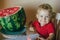Baby Todler sit at a table near a large watermelon and smiles. selective focus