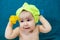 Baby with towel cap on head holding ship toys in hands, portrait after bath, blue background