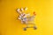 Baby vitamins in the form of bears fell out of the toy carts for products. On a bright yellow background. Pharmaceutical concept