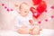 Baby with white feather wings eats heart-shaped cookies, symbols of Valentine`s Day