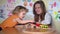 Babysitter and curious toddler girl play with wooden toy train in kindergarten