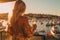 Back beautiful slim chic girl with long blond hair in golden dress with champagne glass in hand background of the bay of yachts in